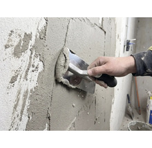 Un artisan applique du plâtre sur un mur avec une truelle.