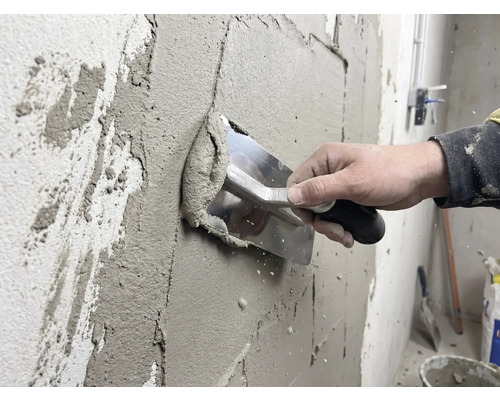 Un artisan applique du plâtre sur un mur avec une truelle.