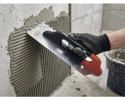 Application de colle à carrelage sur un mur à l'aide d'une truelle en acier inoxydable