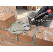 Une main gantée applique du mortier sur un mur de briques avec une truelle