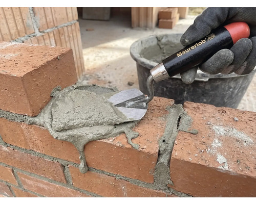 Une main gantée applique du mortier sur un mur de briques avec une truelle