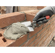 Un maçon applique du mortier sur un mur de briques à l'aide d'une truelle.