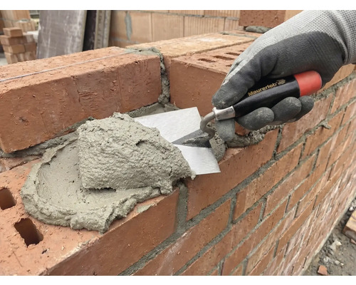 Un maçon applique du mortier sur un mur de briques à l'aide d'une truelle.