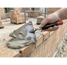 Maurer legt Ziegel mit einer Kelle und Mörtel.