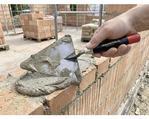 Maurer legt Ziegel mit einer Kelle und Mörtel.