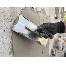 Artisan lissant l'enduit avec une taloche sur un mur.