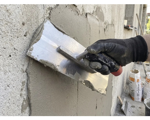 Artisan lissant l'enduit avec une taloche sur un mur.