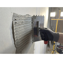 De la colle à carrelage est appliquée sur un mur avec une truelle en acier inoxydable