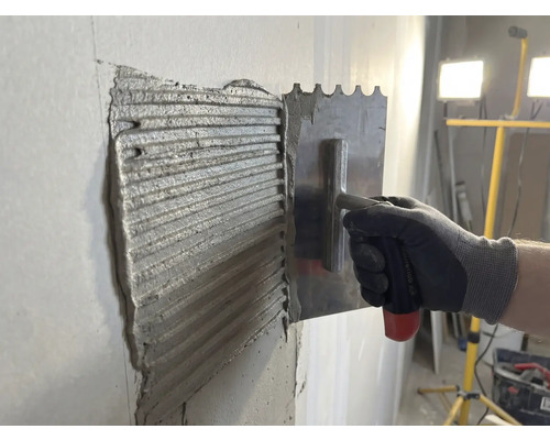 De la colle à carrelage est appliquée sur un mur avec une truelle en acier inoxydable