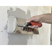 Une personne lisse du plâtre avec une spatule sur un mur.