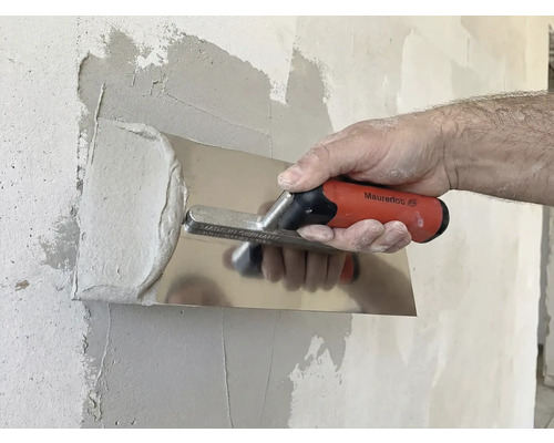 Une personne lisse du plâtre avec une spatule sur un mur.