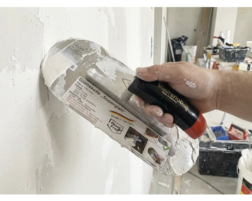 Taloche à lisser Superglatt avec manche dans la main lors du plâtrage d'un mur