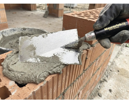 Maurer mit Kelle beim Auftragen von Mörtel auf Ziegelsteine für Mauerbau