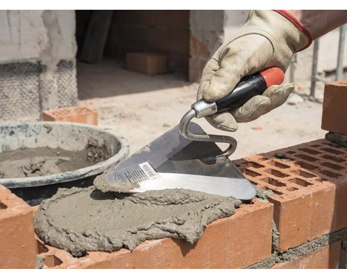 Maurerhand mit Kelle beim Auftragen von Mörtel auf Ziegelsteine