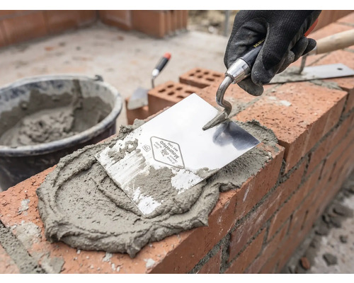 Maçon au travail avec truelle, mortier et briques