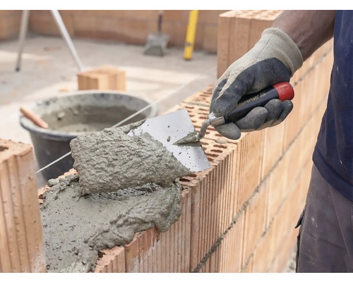 Maçon appliquant du mortier et des briques pour la construction d'un mur
