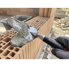 Main de maçon avec truelle appliquant du mortier sur des briques