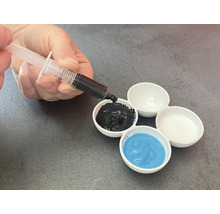 La main remplit un godet de mélange de peinture avec de la peinture noire à l'aide d'une seringue