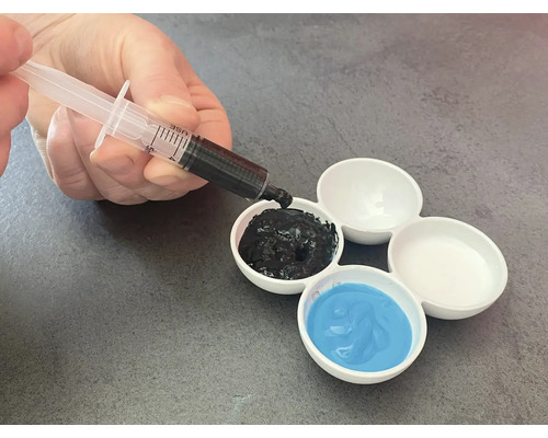 La main remplit un godet de mélange de peinture avec de la peinture noire à l'aide d'une seringue