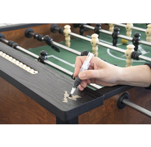 Une personne retouche des rayures sur un baby-foot avec un stylo de retouche.