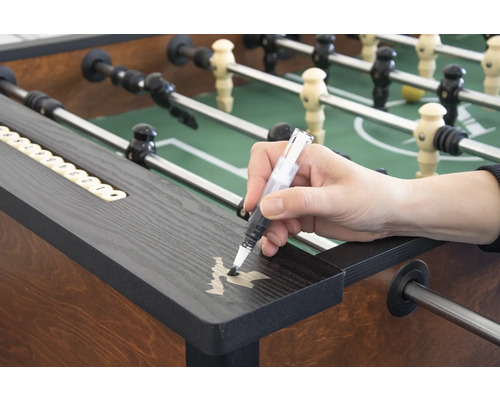 Une personne retouche des rayures sur un baby-foot avec un stylo de retouche.