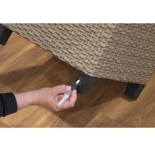 Une personne répare un meuble en rotin avec un stylo de retouche.