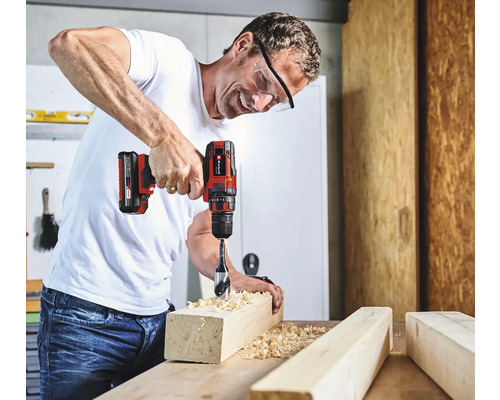 Un homme perce un trou dans une pièce de bois avec une perceuse-visseuse sans fil