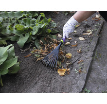 Une personne ratisse les feuilles avec un balai à gazon dans le jardin.