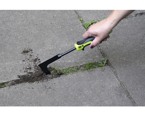Une main utilise un couteau à joints pour enlever les mauvaises herbes entre les pavés.