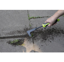 Une personne enlève les mauvaises herbes avec un désherbeur de joints sur une surface pavée.