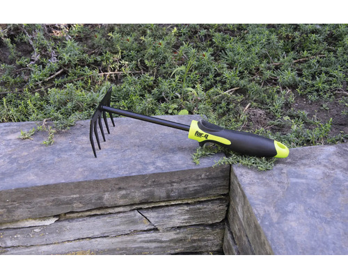 Râteau à feuilles et de jardin avec dents et manche en plastique sur mur de pierre