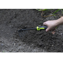 Une main tient une petite houe dans la terre du jardin
