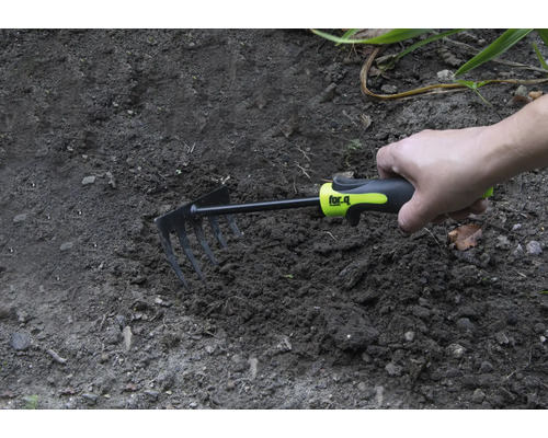 Une main tient une petite houe dans la terre du jardin