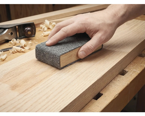 Main ponçant une planche de bois avec un tampon abrasif sur une cale à poncer.
