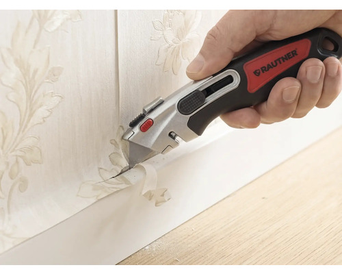 Main avec un cutter Rautner coupant avec précision du papier peint à motif floral le long d une plinthe.