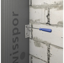 Ein Schraubendreher fixiert eine Metallplatte an einer grauen Bauplatte an einer weißen Mauer.