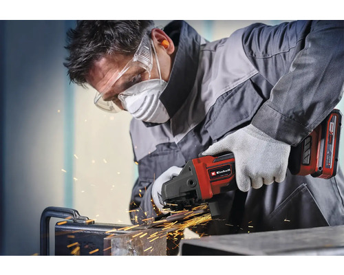 Handwerker arbeitet mit Einhell Akku-Winkelschleifer an Metall mit Funkenflug, trägt Schutzbrille, Atemschutzmaske, Gehörschutz und Handschuhe.