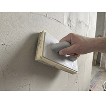 Main utilisant une taloche éponge de 28 par 14 centimètres pour lisser l'enduit frais sur un mur.