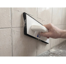 Personne jointoyant des carreaux muraux avec une taloche à joints en plastique et caoutchouc mousse.