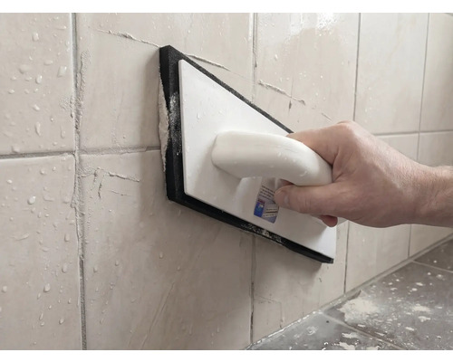 Personne jointoyant des carreaux muraux avec une taloche à joints en plastique et caoutchouc mousse.