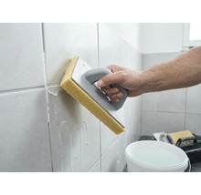 Eine Person reinigt frisch verfugte Wandfliesen mit einem Schwammbrett und Wasser.