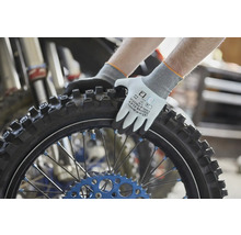 Gebol Aarbechtshandschuhen Master Flex Cool an Touch beim Festhalten vun engem Motorradspneu mat Stollenprofil an engem Atelier.