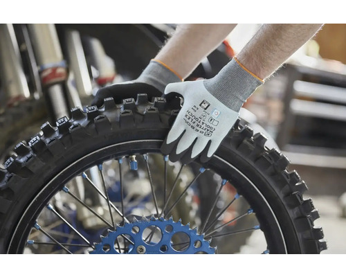 Gebol Aarbechtshandschuhen Master Flex Cool an Touch beim Festhalten vun engem Motorradspneu mat Stollenprofil an engem Atelier.