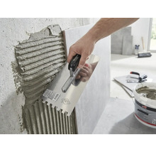 Une main applique de la colle à carrelage sur un mur à l'aide d'une truelle dentelée.