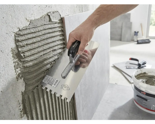 Une main applique de la colle à carrelage sur un mur à l'aide d'une truelle dentelée.