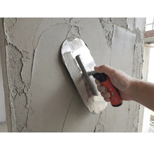 Une taloche appliquant de l'enduit gris sur un mur.