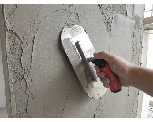 Une taloche appliquant de l'enduit gris sur un mur.