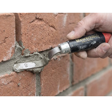 Une personne utilise une truelle à joints Maurerlob pour appliquer du mortier entre des briques rouges.