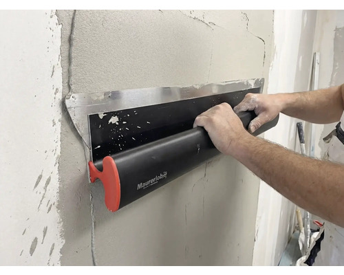 Eng Persoun benotzt eng Maurerlob Flächenspachtel fir fiichte Putz op enger Mauer glat ze sträichen.