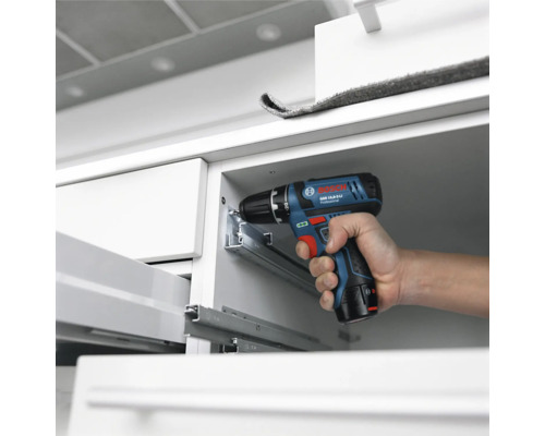Perceuse-visseuse sans fil Bosch Professional installant des glissières de tiroir en métal dans un meuble blanc.